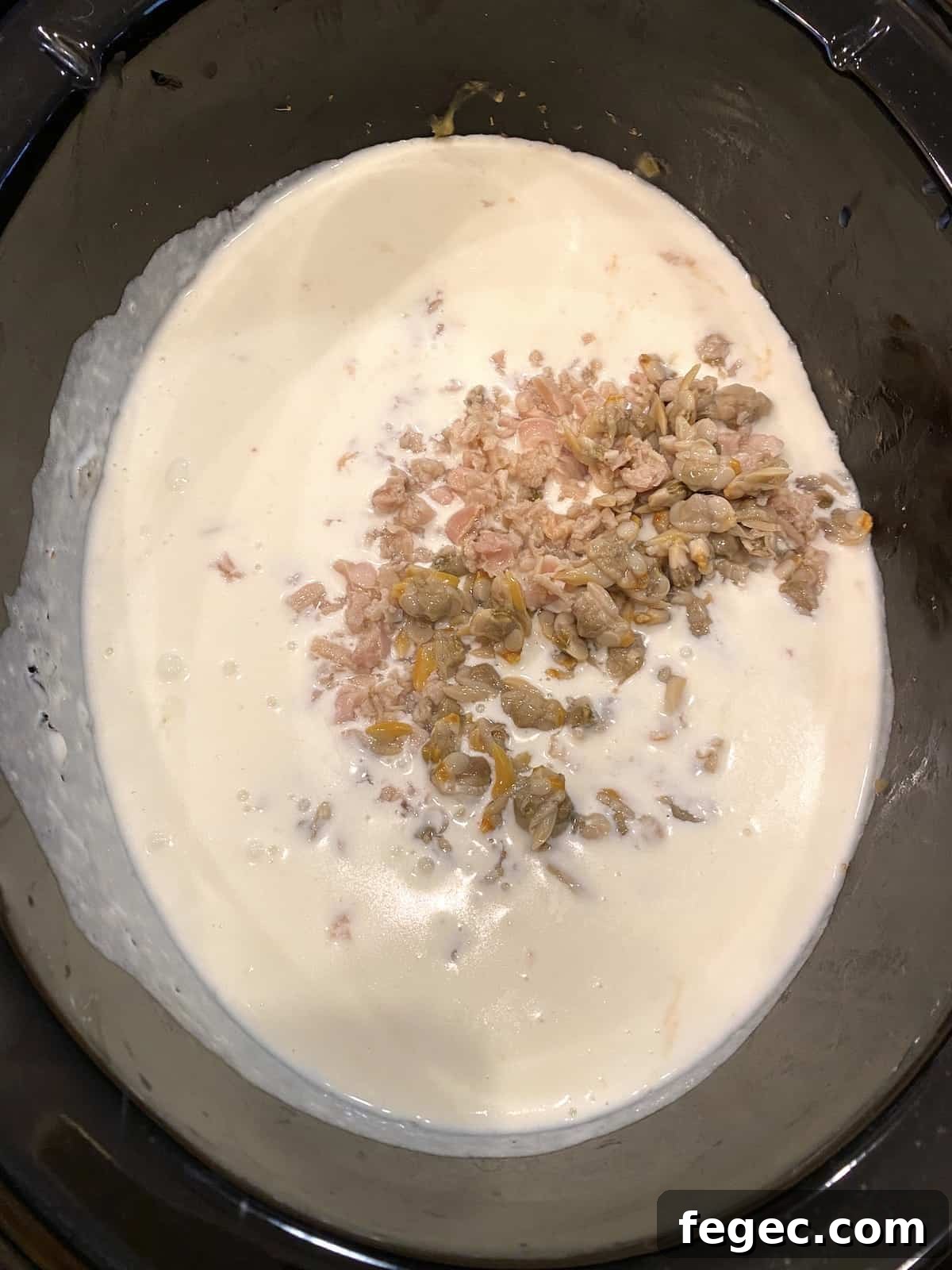 Clams placed on top of the white sauce in a crockpot.