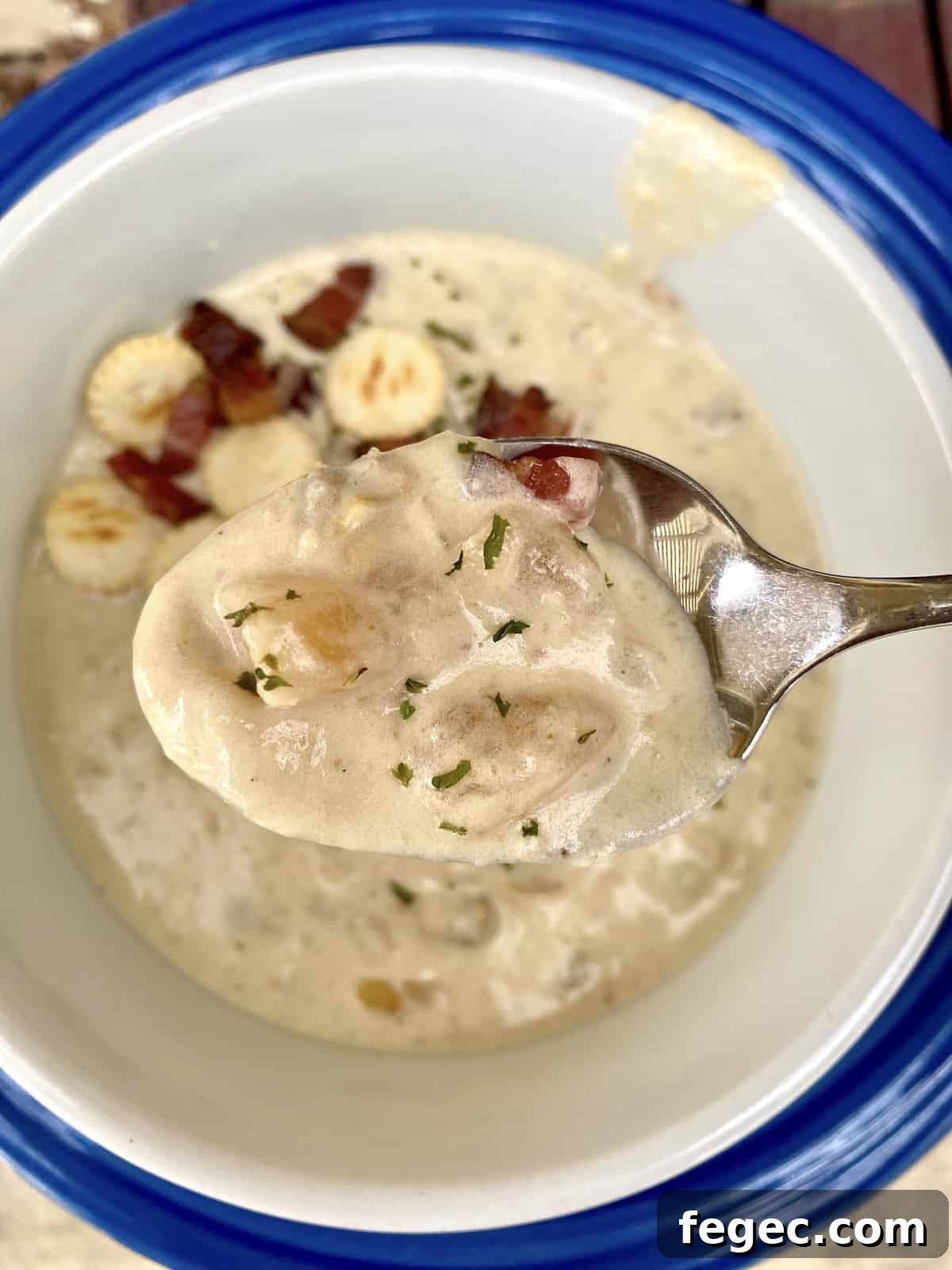 A spoonful of clam chowder, with crackers and bacon bits on the surface of the chowder in the bowl.