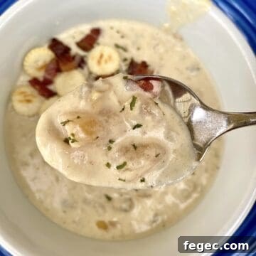 A spoonful of clam chowder, with crackers and bacon bits on the surface of the chowder in the bowl.