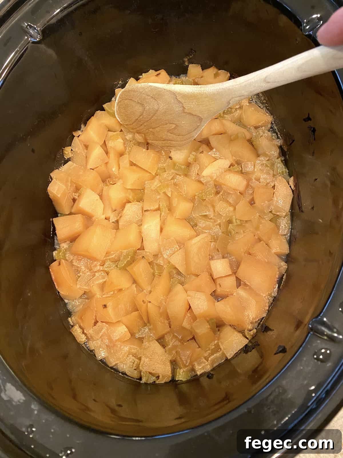 Cooked potatoes and celery in a crockpot with a wooden spoon on the side of the pot.