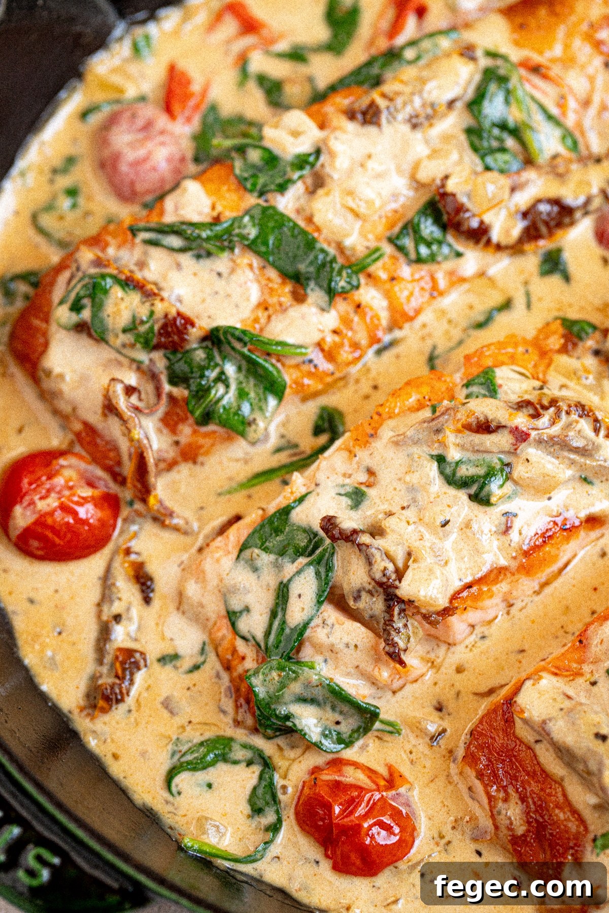 Two pieces of salmon in a cast iron skillet sitting in a creamy tuscan sauce.