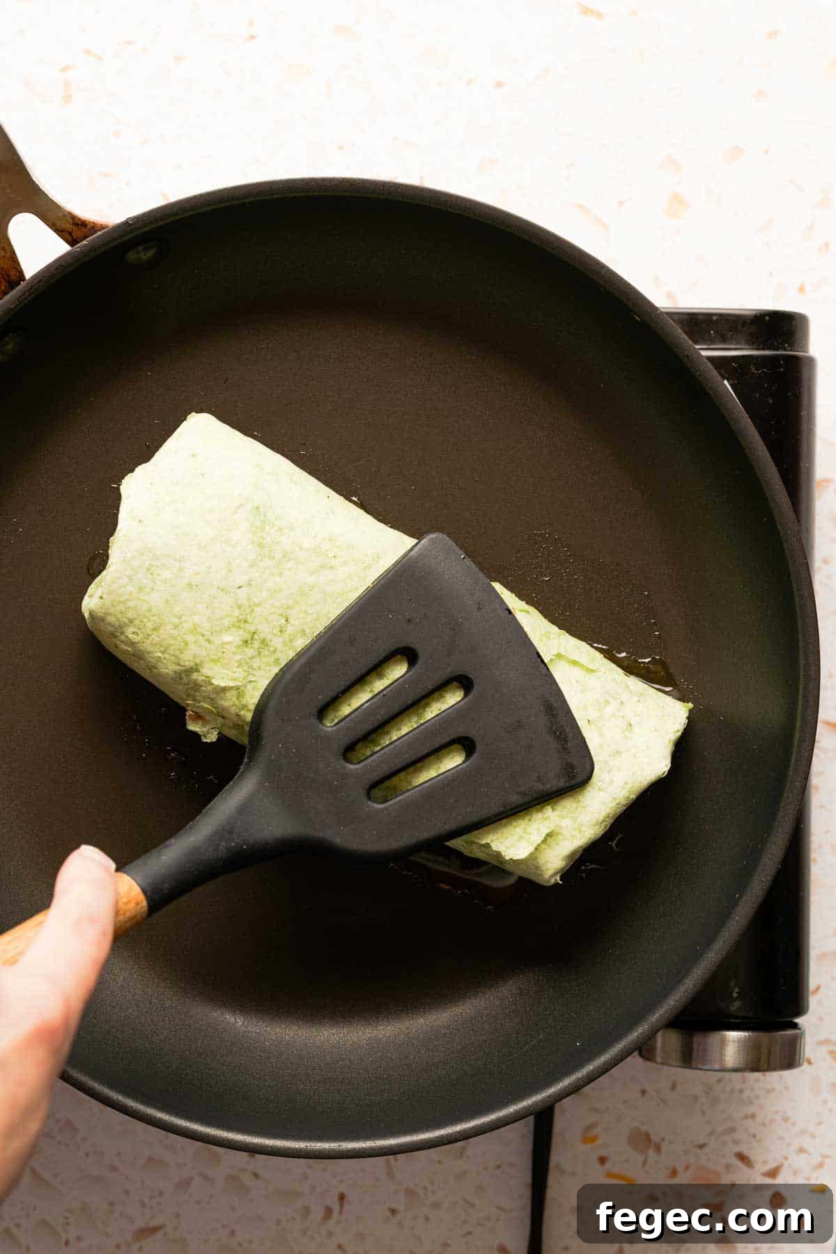 Crispy Tuna Melt Wrap Recipe for Quick Lunch or Picnic 13 tuna melt wrap being pressed down in pan with spatula.