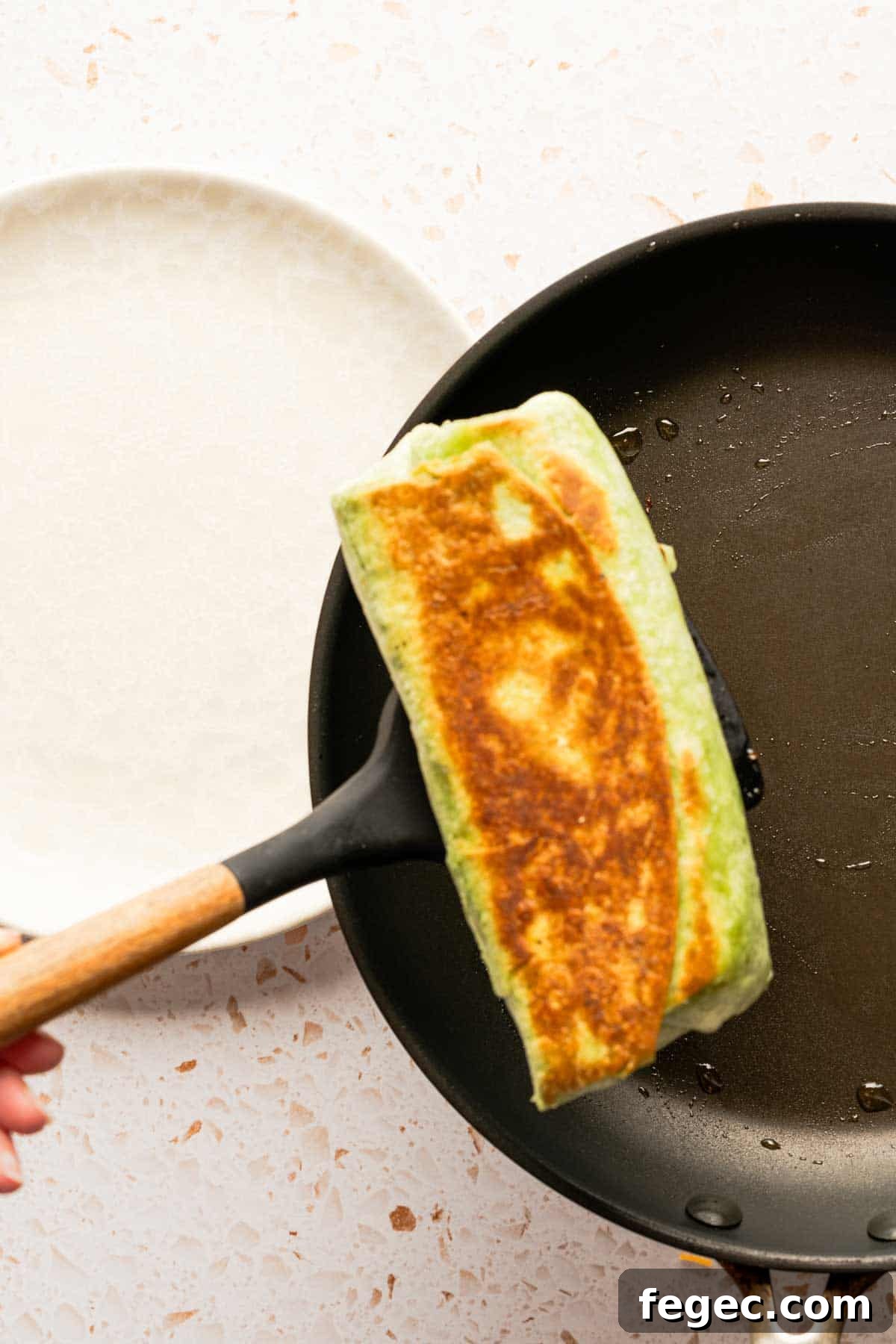 Crispy Tuna Melt Wrap Recipe for Quick Lunch or Picnic 15 spatula moving browned sandwich wrap from pan to plate.