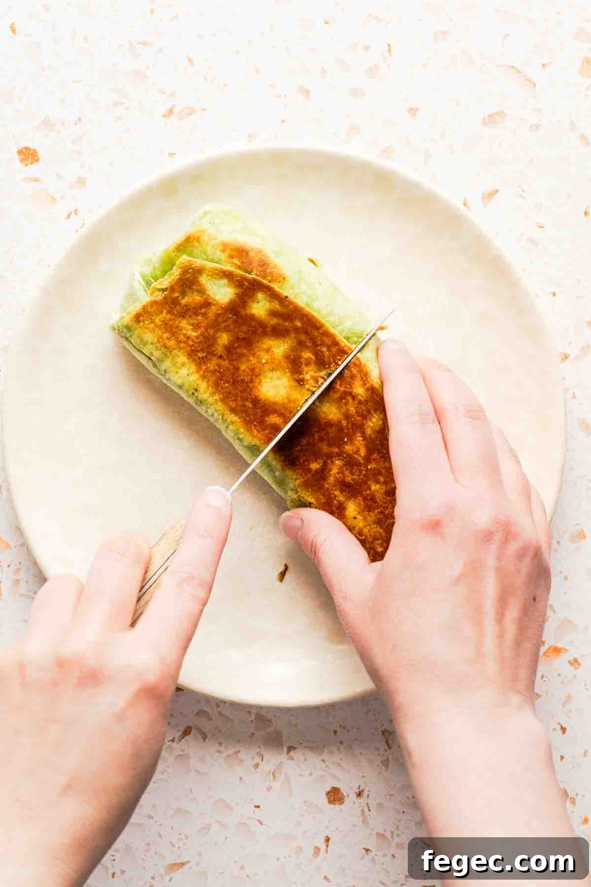 Crispy Tuna Melt Wrap Recipe for Quick Lunch or Picnic 16 wrap sandwich being cut in half on white plate.
