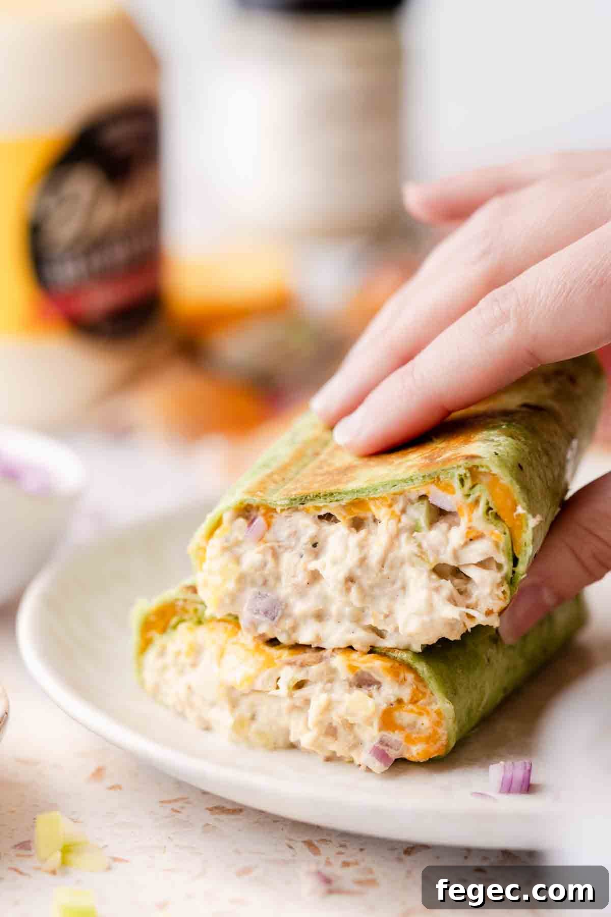 Crispy Tuna Melt Wrap Recipe for Quick Lunch or Picnic 17 hand picking up half of tuna melt wrap stacked on plate.