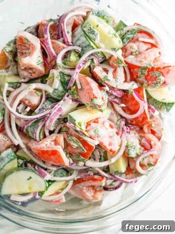creamy cucumber tomato and onion salad in large glass bowl.