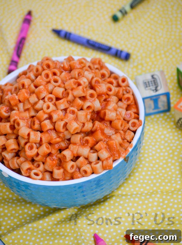 Homemade Spaghetti O's in a white rimmed blue bowl on a yellow background with crayons and wooden toy blocks