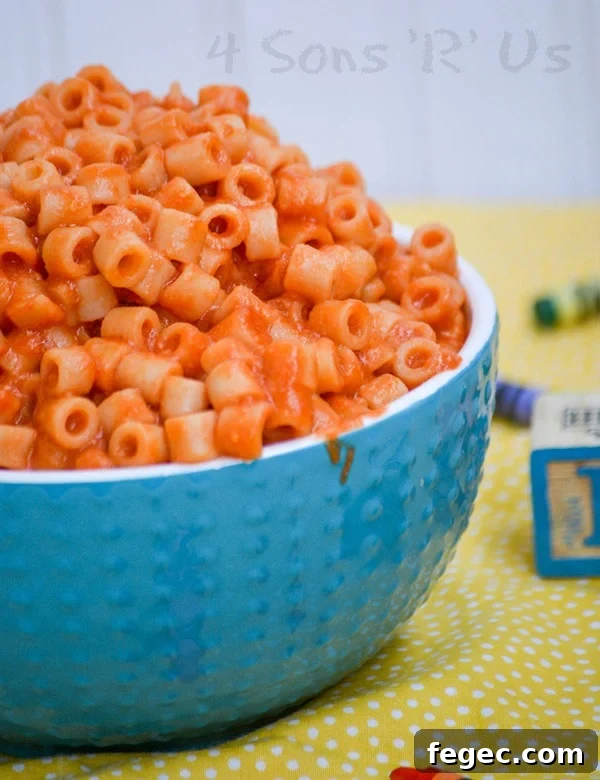 Homemade Spaghetti O's in a white rimmed blue bowl on a yellow background with crayons and wooden toy blocks