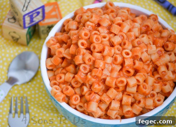 Homemade Spaghetti O's in a white rimmed blue bowl on a yellow background with crayons and wooden toy blocks