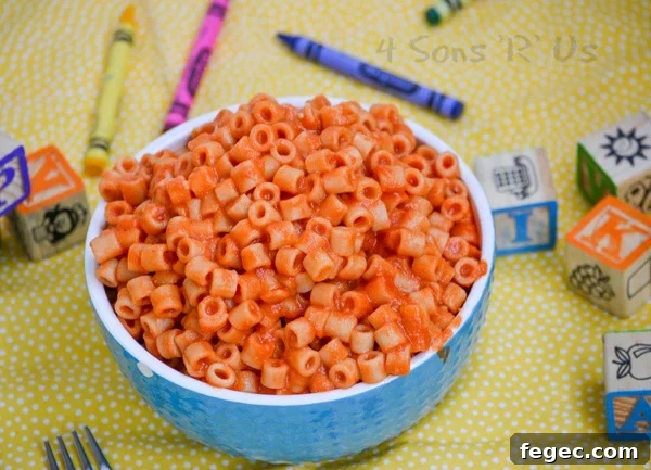 Homemade Spaghetti O's in a white rimmed blue bowl on a yellow background with crayons and wooden toy blocks