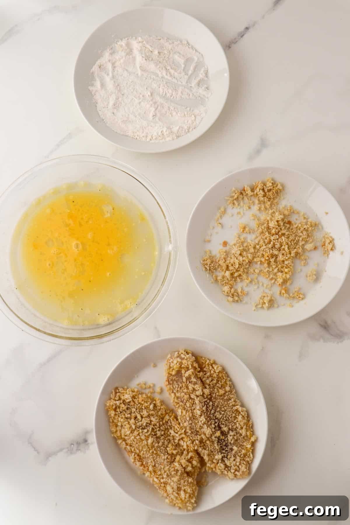 Flour, beaten egg, panko bread crumbs and breaded fish on separate plates.