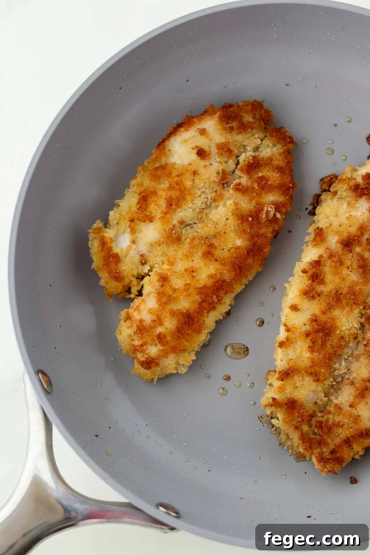 Breaded pan-fried fish in a gray skillet.