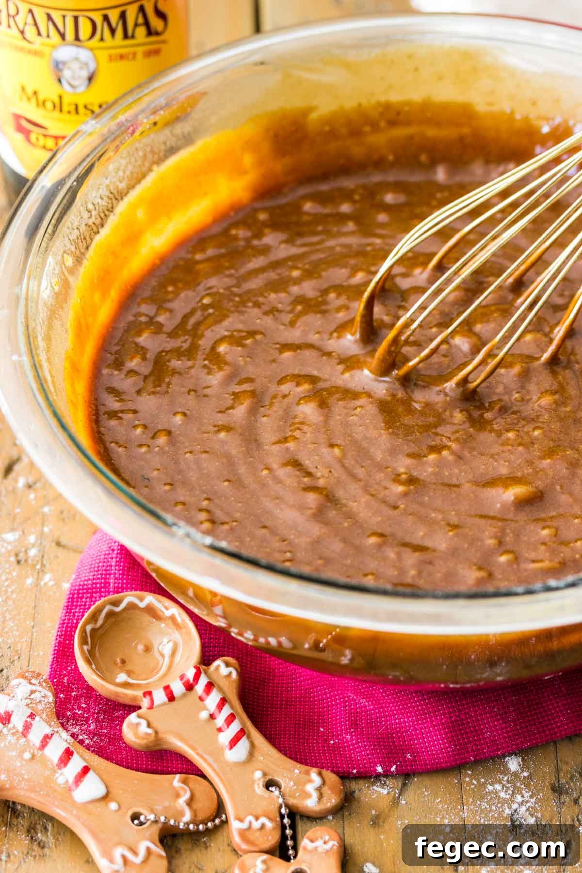 Gingerbread batter being whisked in a glass bowl with two gingerbread cookie shaped measuring spoons in foreground