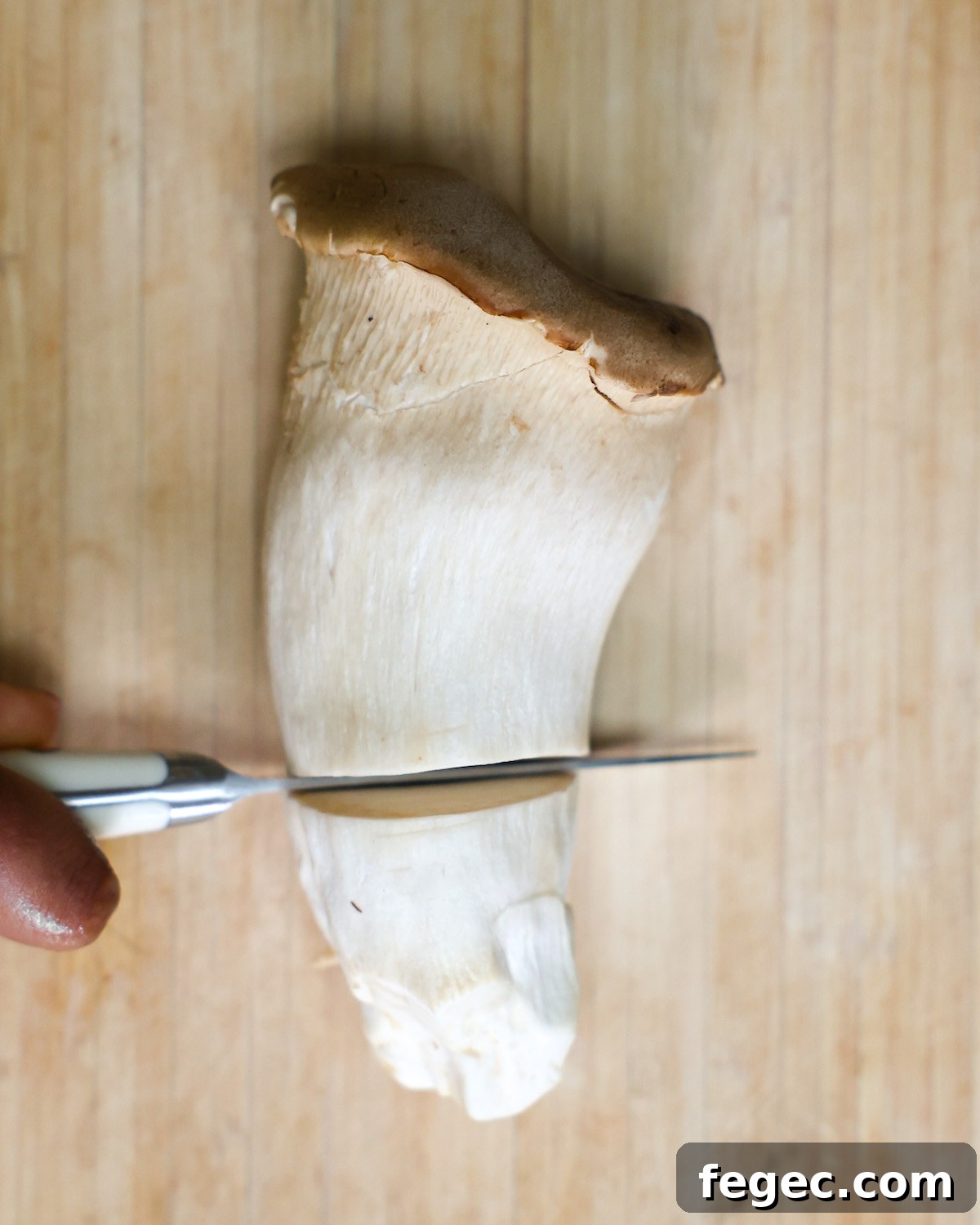 Paring knife slicing through a large king oyster mushroom.