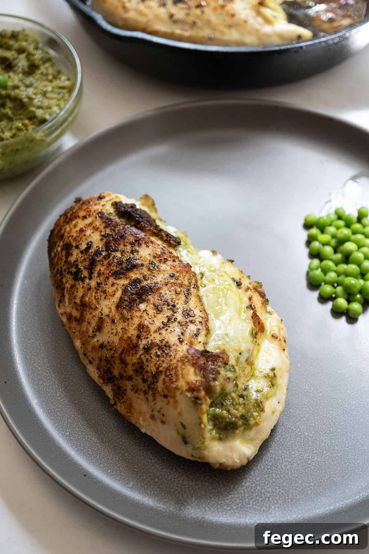 Pesto stuffed chicken on a plate with peas.