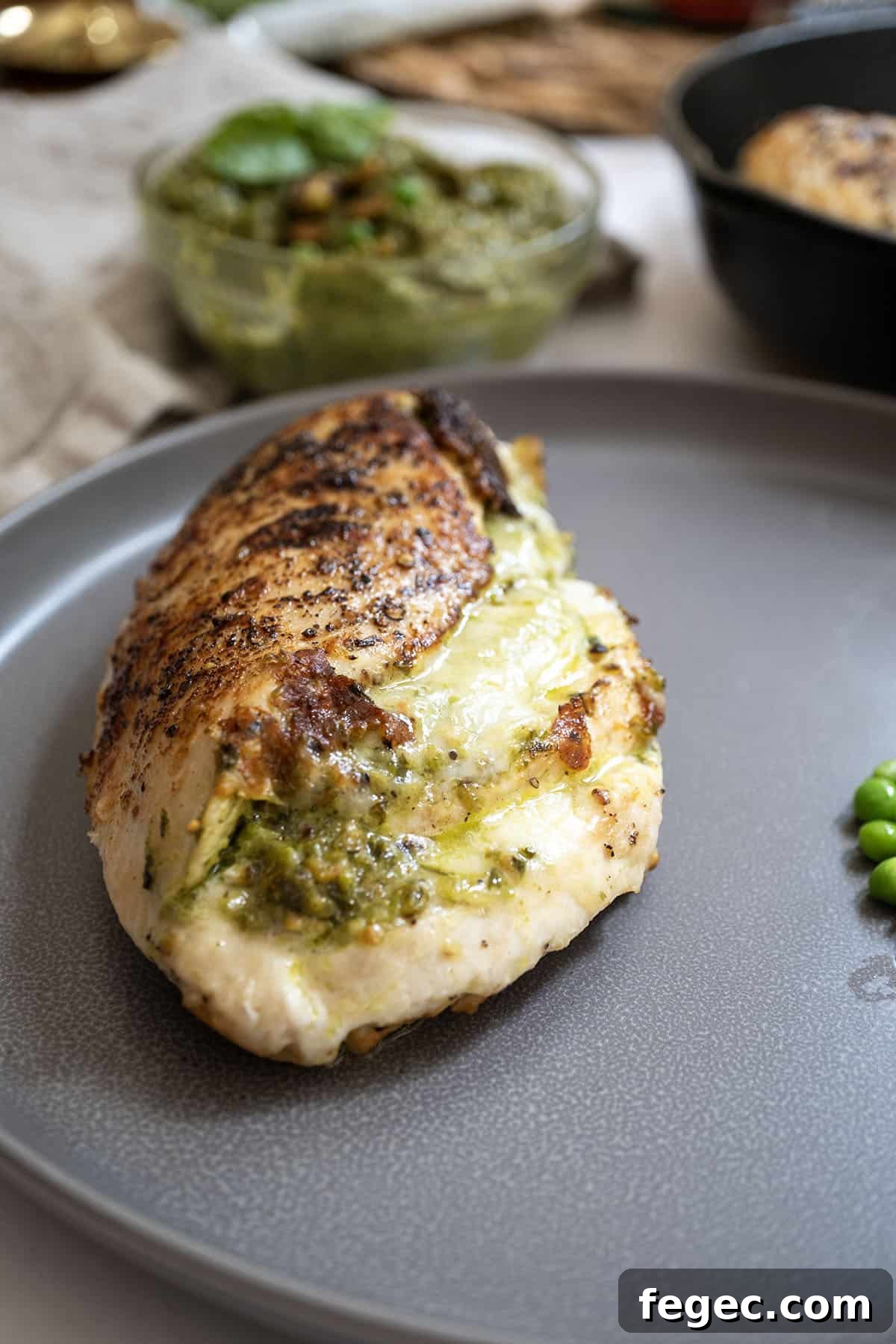 Pesto stuffed chicken on a plate with peas.