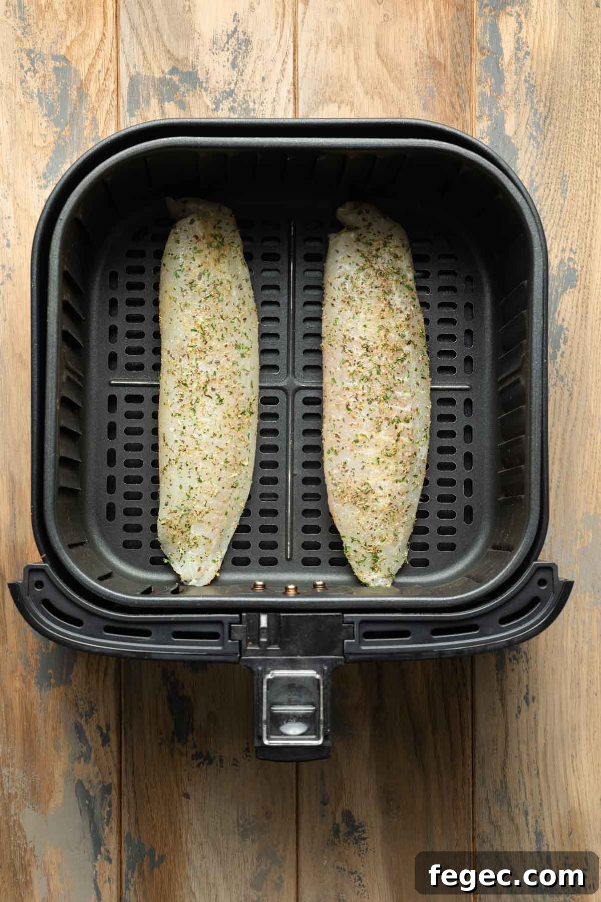 Seasoned tilapia loins in an air fryer basket.