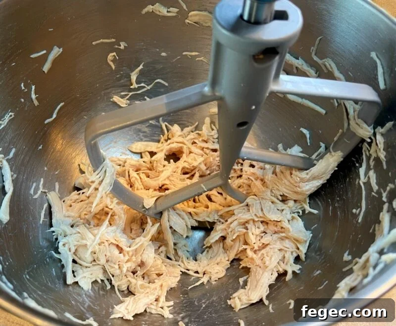 cooked chicken being shredded in a stand mixer