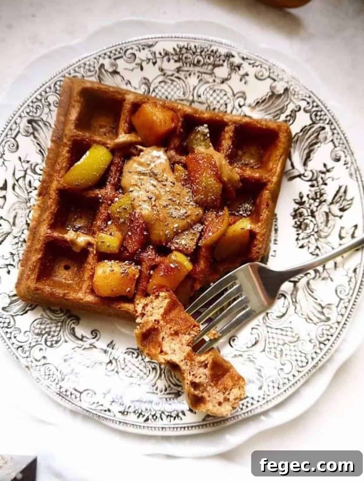 Apple cinnamon waffles on a plate with apples on top.