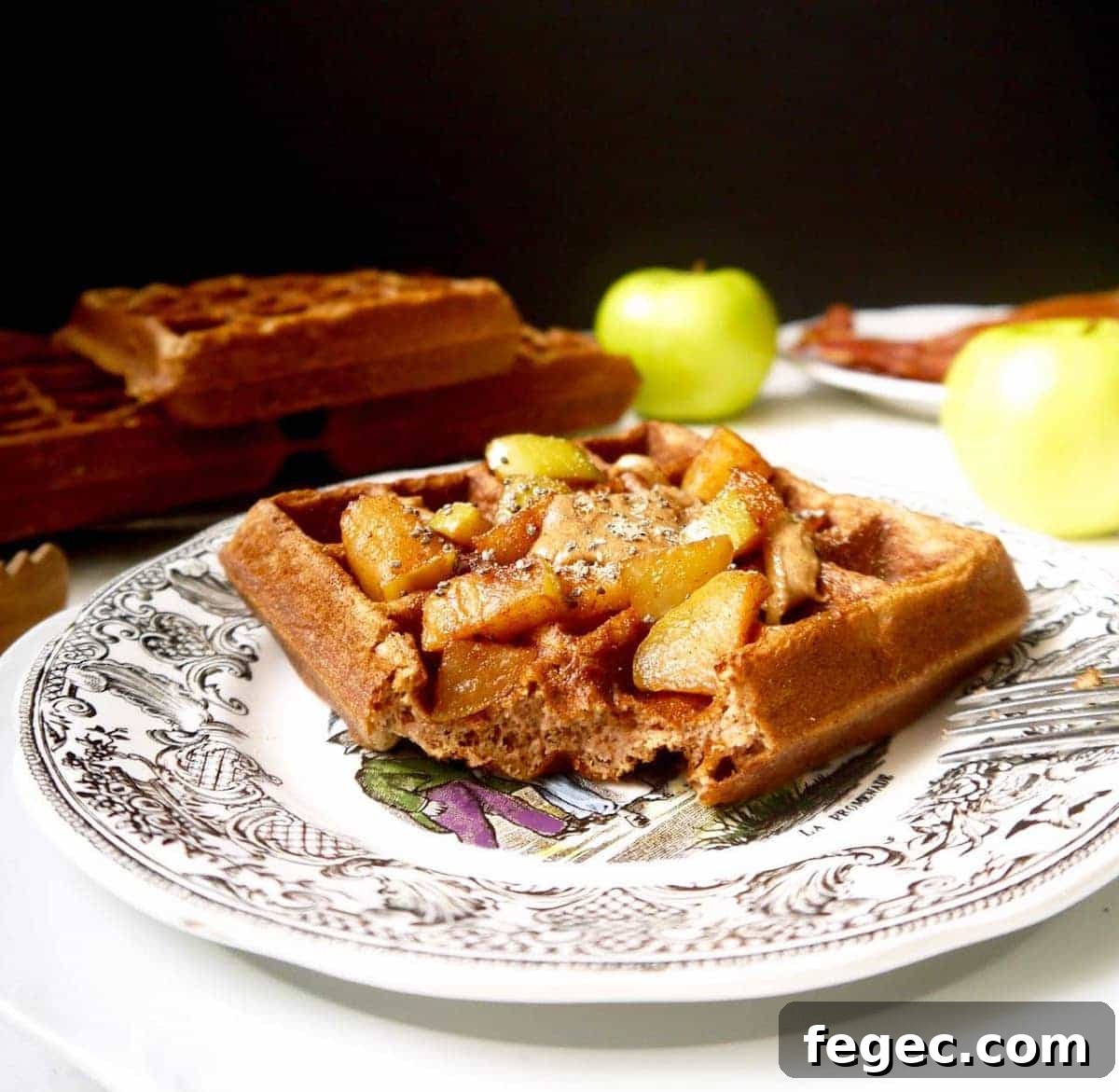 Gluten free apple cinnamon waffles on a plate with a bite taken out of it.