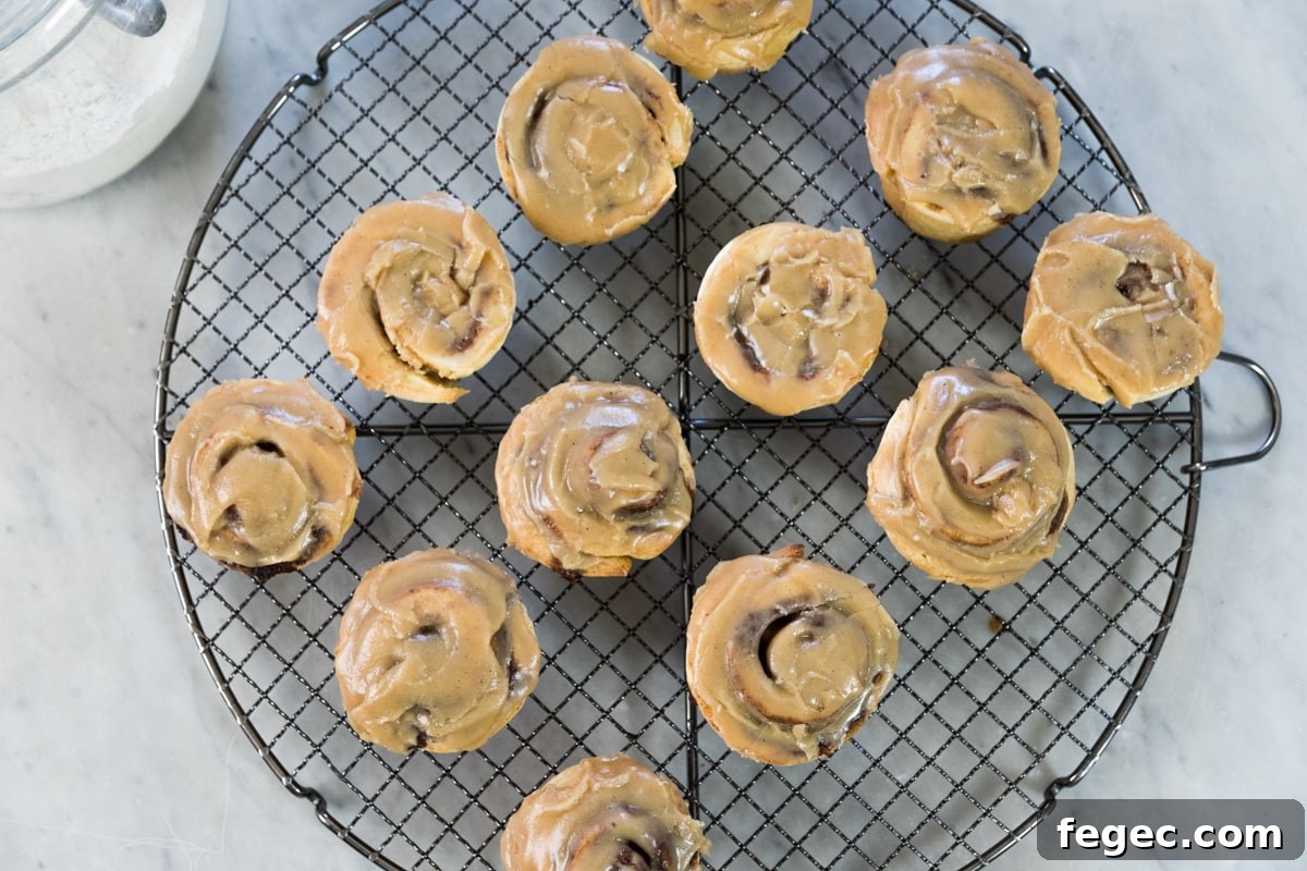 Top down view of circular cooling rack holding cooling cinnamon roll muffins topped with brown sugar glaze