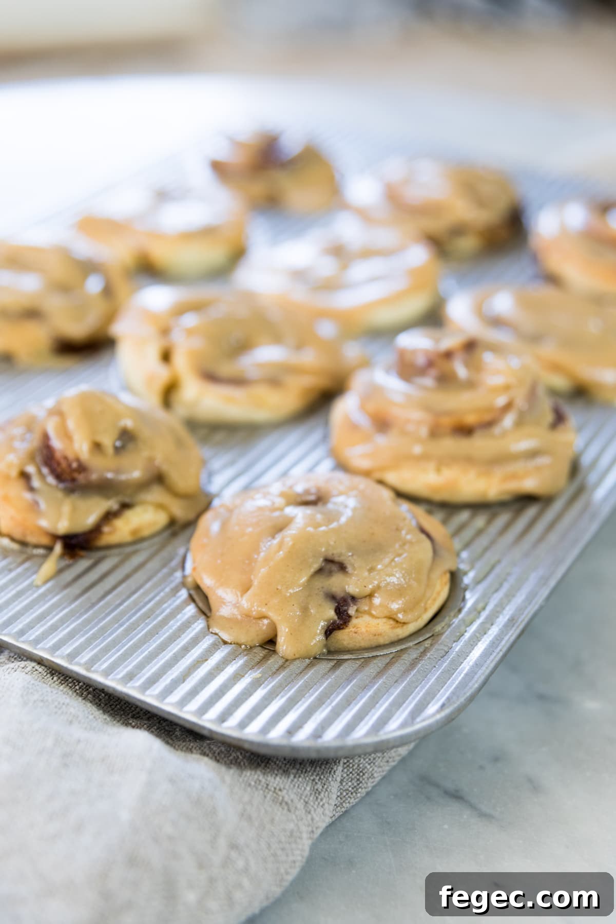 Silver muffin tin filled with cinnamon roll muffins swirled with cinnamon and glazed with a brown sugar icing