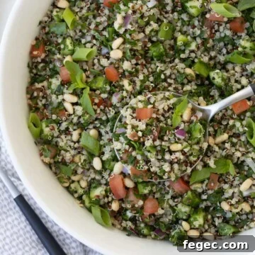 A close up of tabouli salad with tomatoes and green onion in a white bowl.