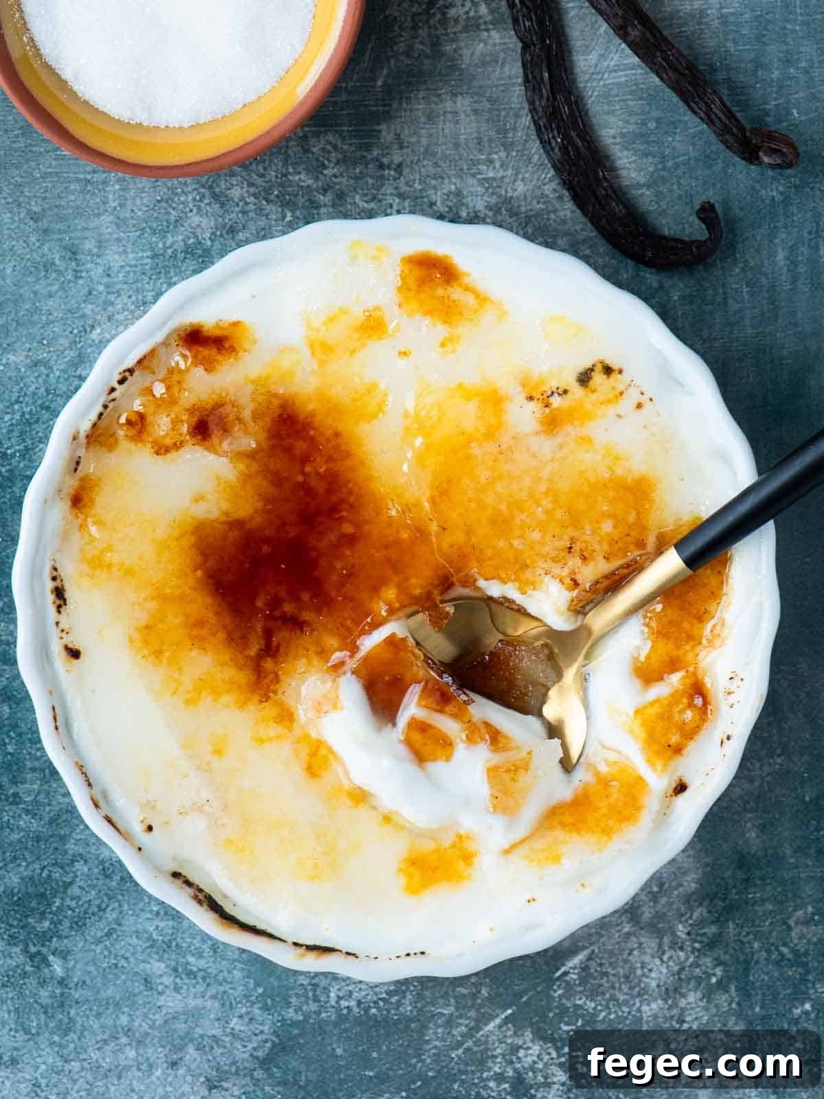 Overhead of creme brulee on a blue surface with a spoon in it.