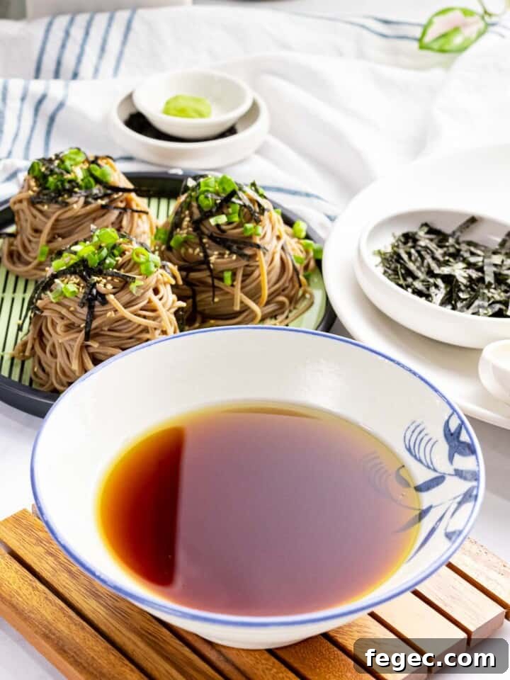 Cold soba noodle dipping sauce in a bowl next to soba noodles.