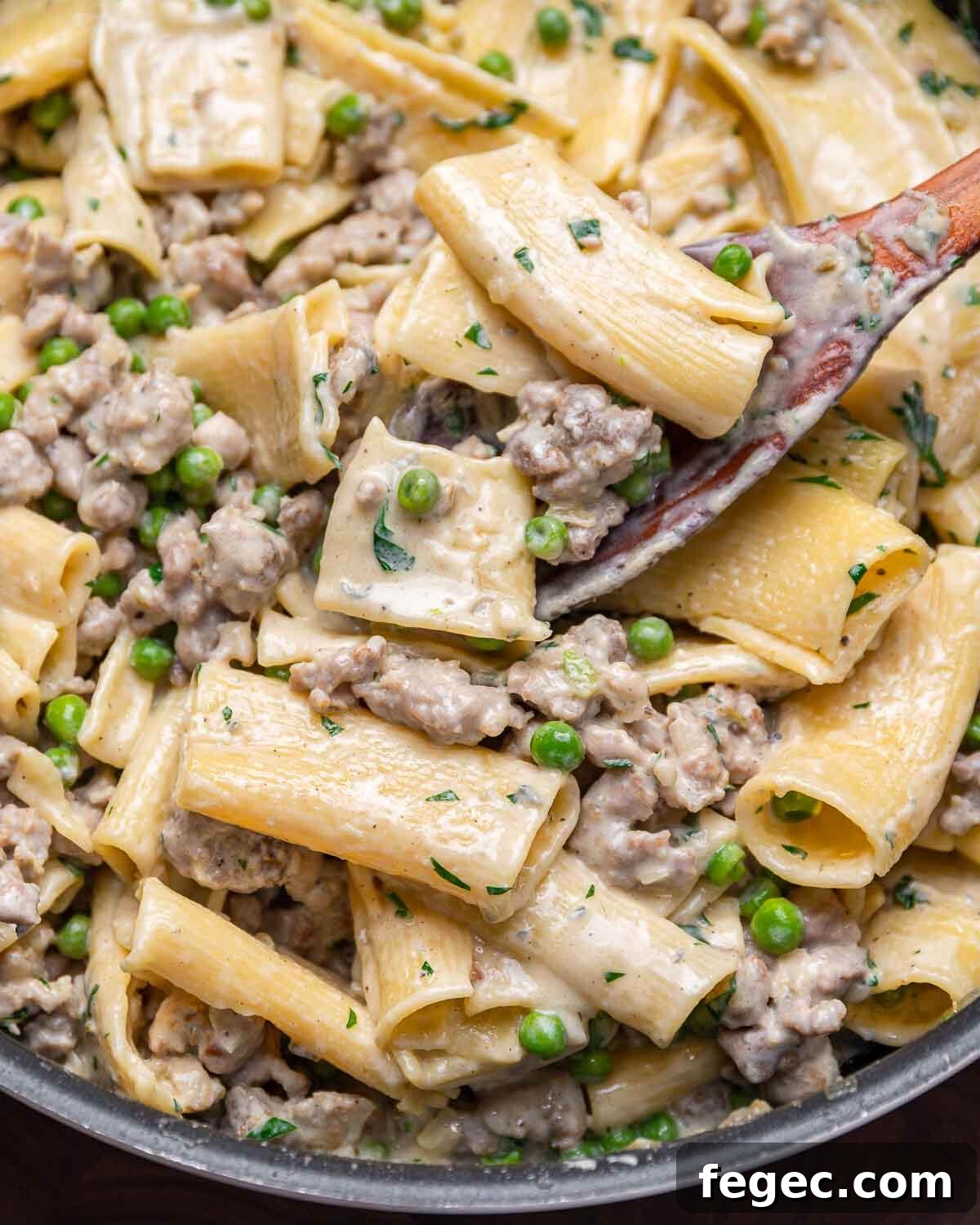 Wooden spoon scooping out gorgonzola cream sauce pasta from large pan.