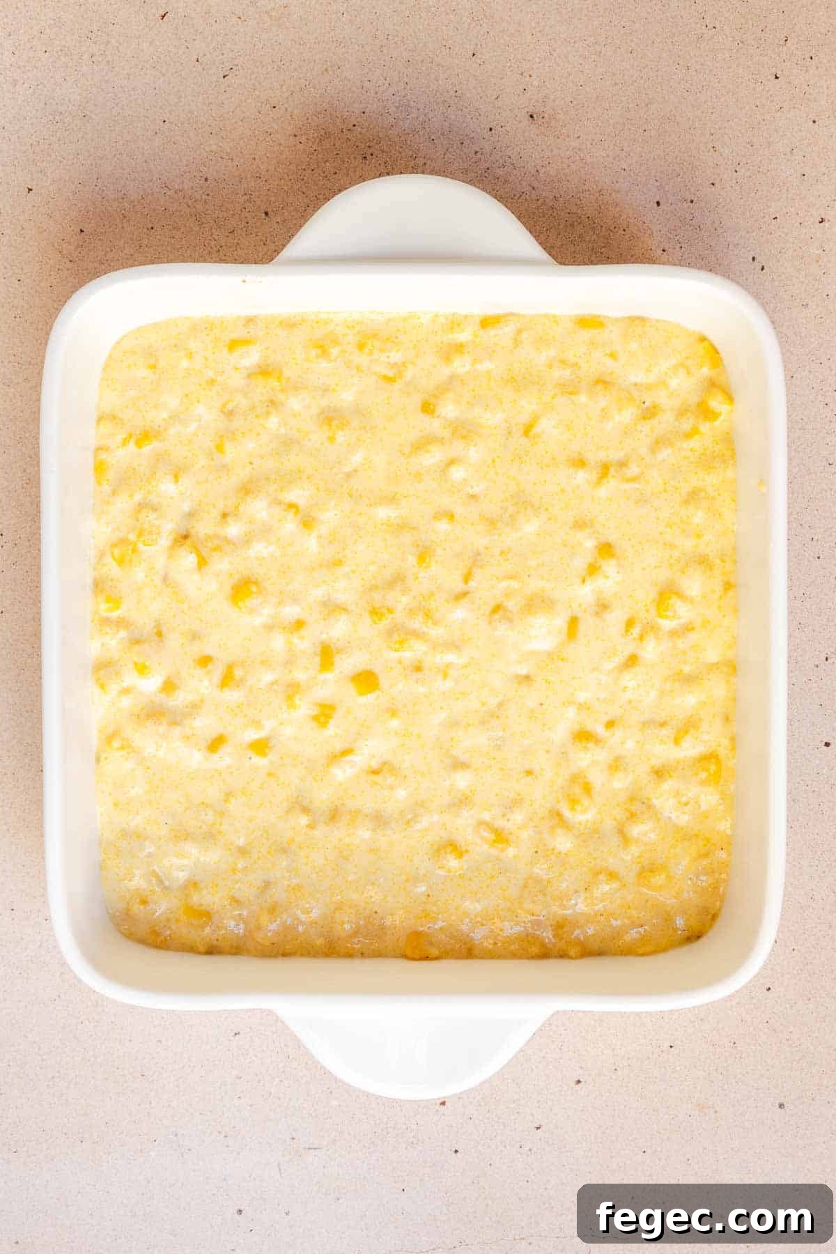 The cornbread mixture is spread evenly in the bottom on an 8 by 8 inch baking dish.
