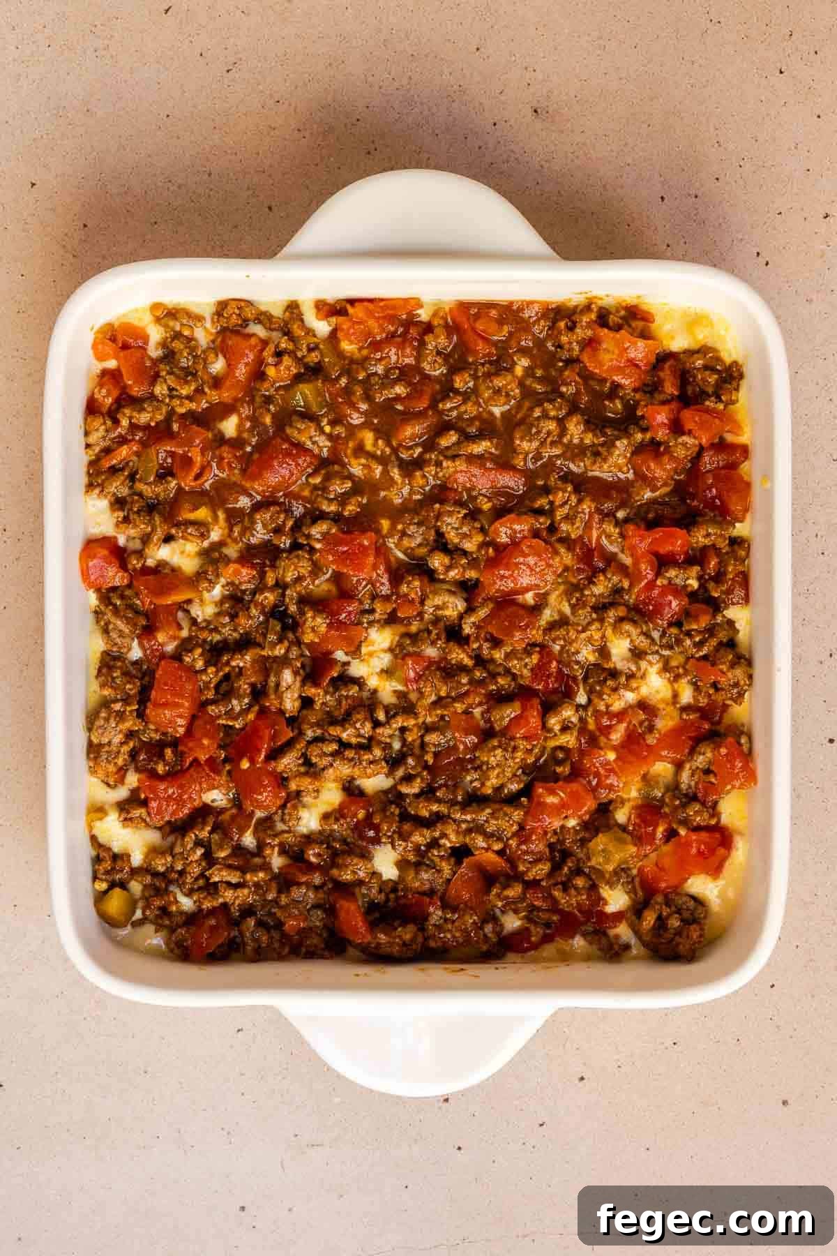 The ground beef mixture is spread evenly over top of the cornbread layer in the 8 by 8 inch baking dish.