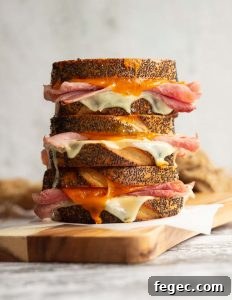 3 sandwiches stacked on each other with ham and cheese dripping out on wooden board