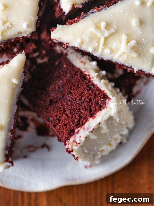 Sliced red velvet cake with cream cheese frosting on a scalloped edge dessert plate with red plaid background.