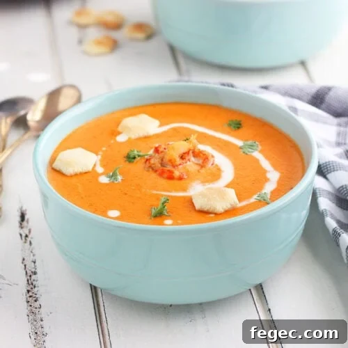 Bowl of crawfish bisque garnished with cream, parsley and oyster crackers on a white wooden background.
