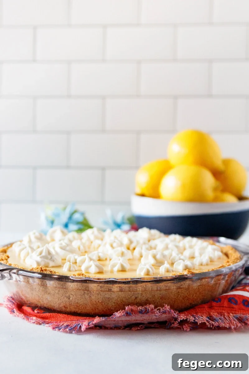 ready to slice lemon pie on a colorful napkin. There's a bowl of lemons in the background and the pie is dotted with swirls of whipped cream
