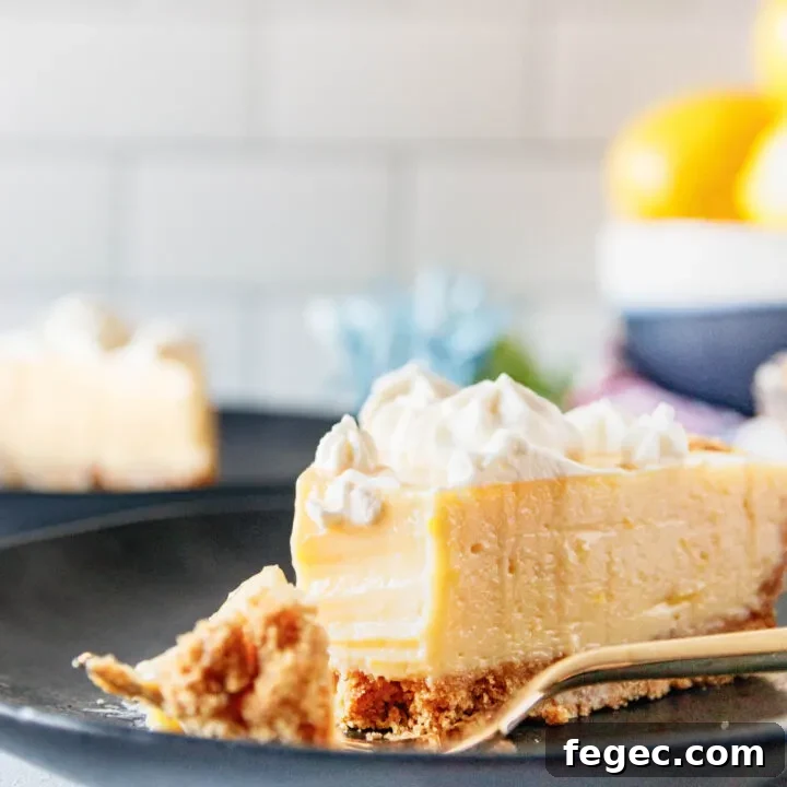 close up picture of a slice of creamy lemon pie with a bite cut out of it. This shows the smooth texture of the pie filling and the contrast with a par-baked graham cracker crust