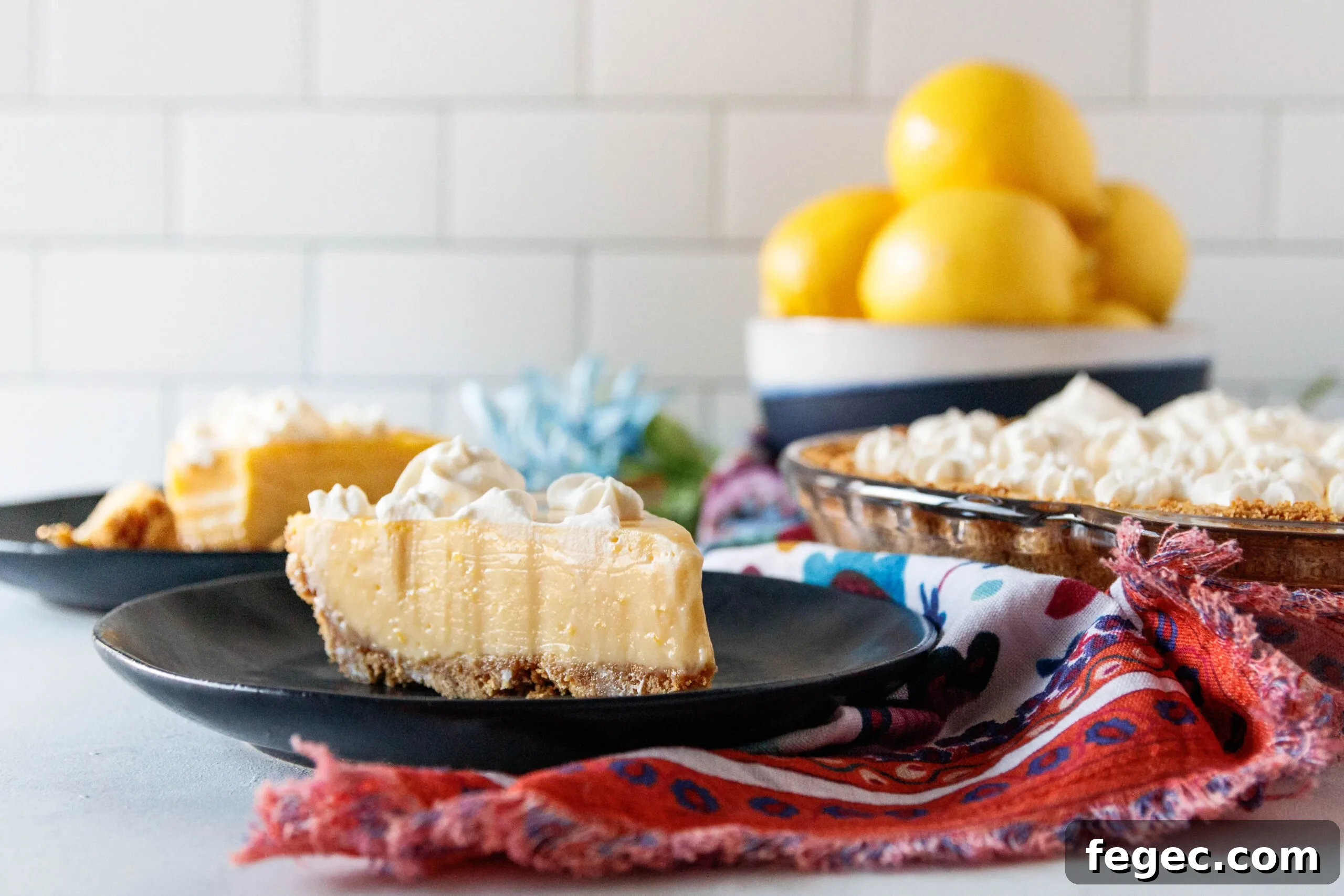 horizontal image showing a slice of lemon pie on a black plate with a bowl of lemons in the background