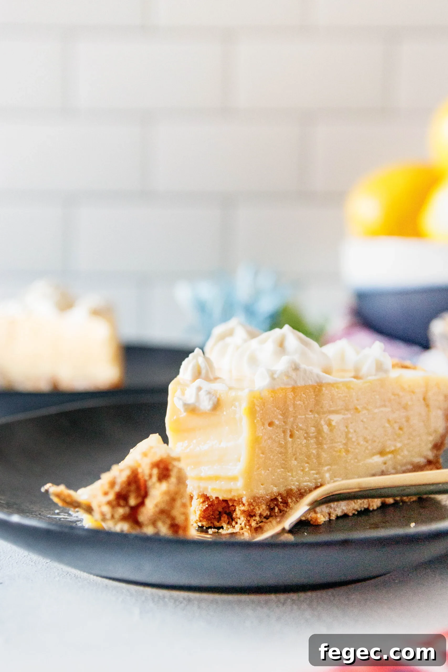 close up picture of a slice of creamy lemon pie with a bite cut out of it. This shows the smooth texture of the pie filling and the contrast with a par-baked graham cracker crust