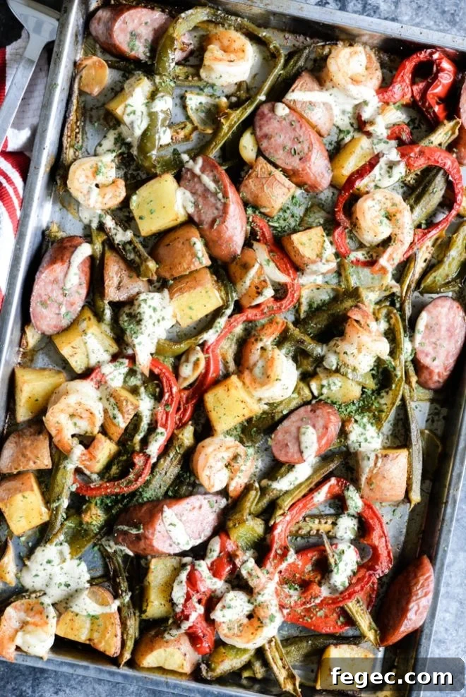 overhead view of a sheet pan loaded with sausage, shrimp, potatoes, asparagus, and red bell peppers with a creamy sauce drizzled over it
