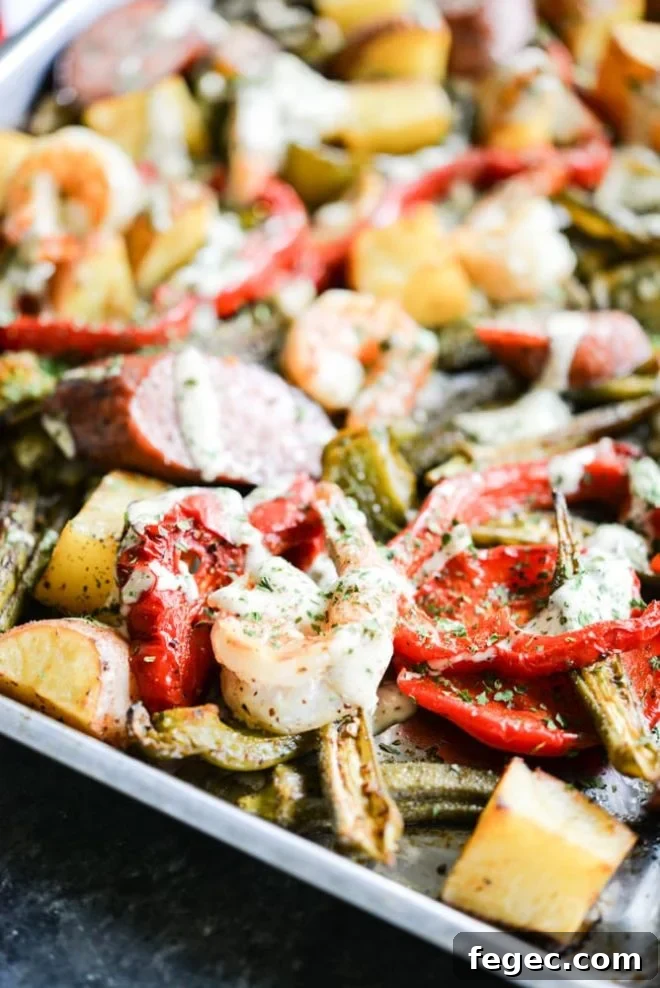 a sheet pan loaded with sausage, shrimp, potatoes, asparagus, and red bell peppers with a creamy sauce drizzled over it