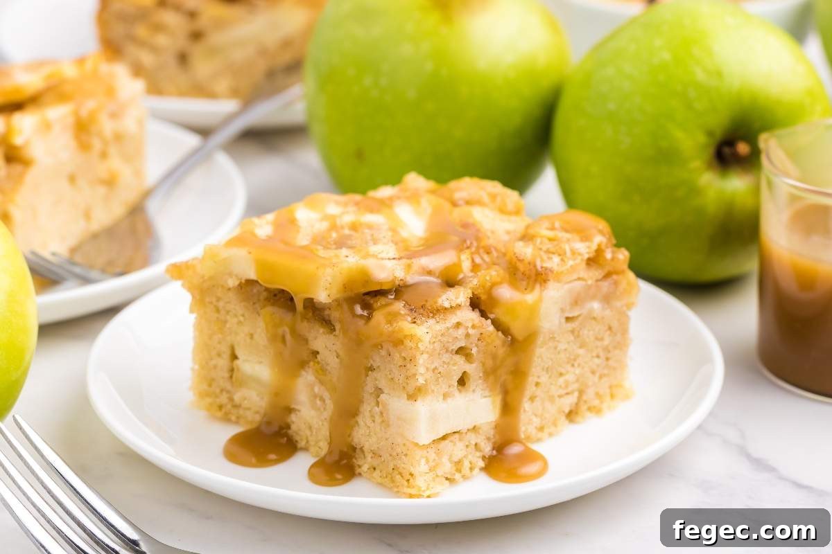 A slice of caramel apple sheet cake on a white plate with a caramel drizzle, accompanied by fresh green apples in the background.