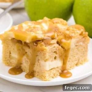 A slice of apple sheet cake with caramel sauce drizzled on top, served on a white plate with whole green apples and a glass of caramel sauce in the background.