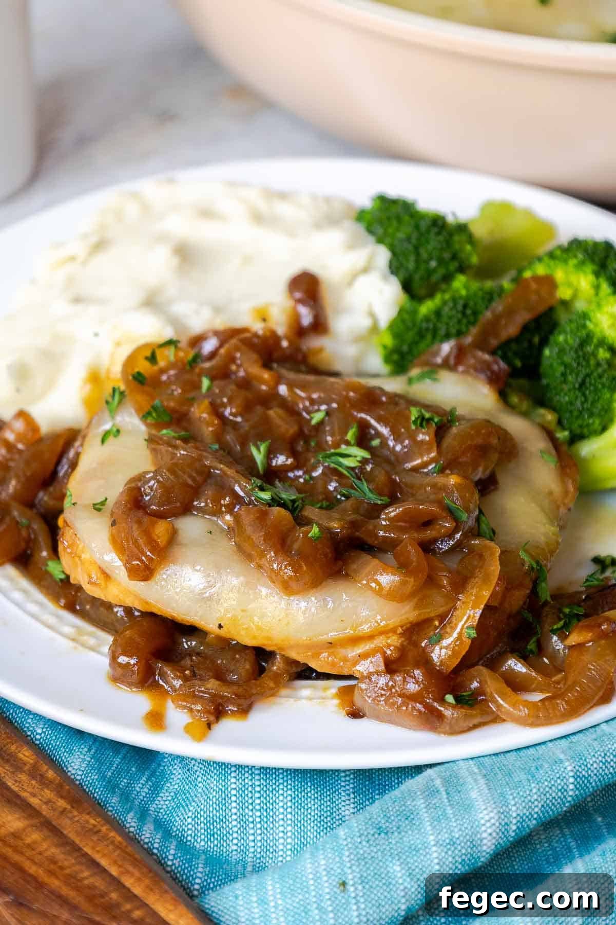 French Onion Pork Chops with Melted Gruyère and Caramelized Onions 2 A pork chop on a plate covered in caramelized onions and cheese with mashed potatoes and broccoli.