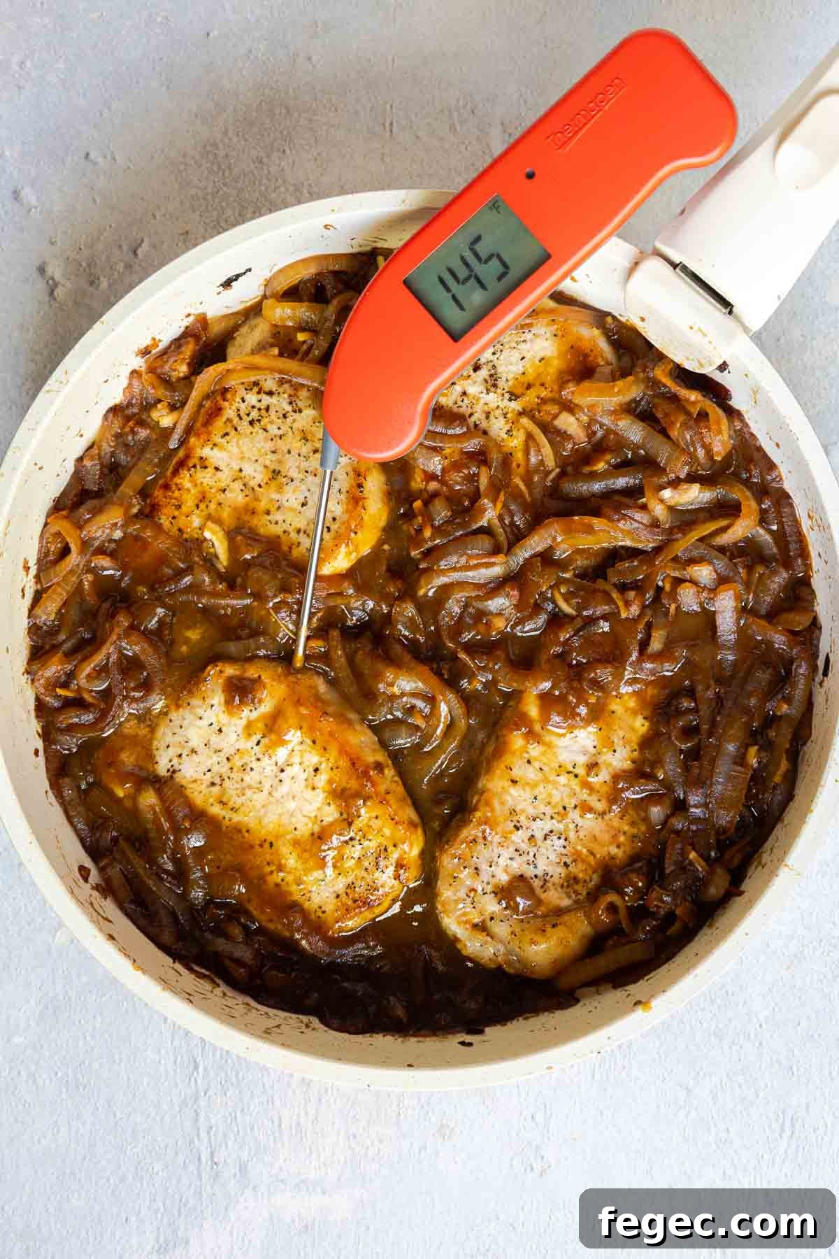 French Onion Pork Chops with Melted Gruyère and Caramelized Onions 11 A meat thermometer in a pork chop showing 145°F, with the chops simmering in caramelized onions.