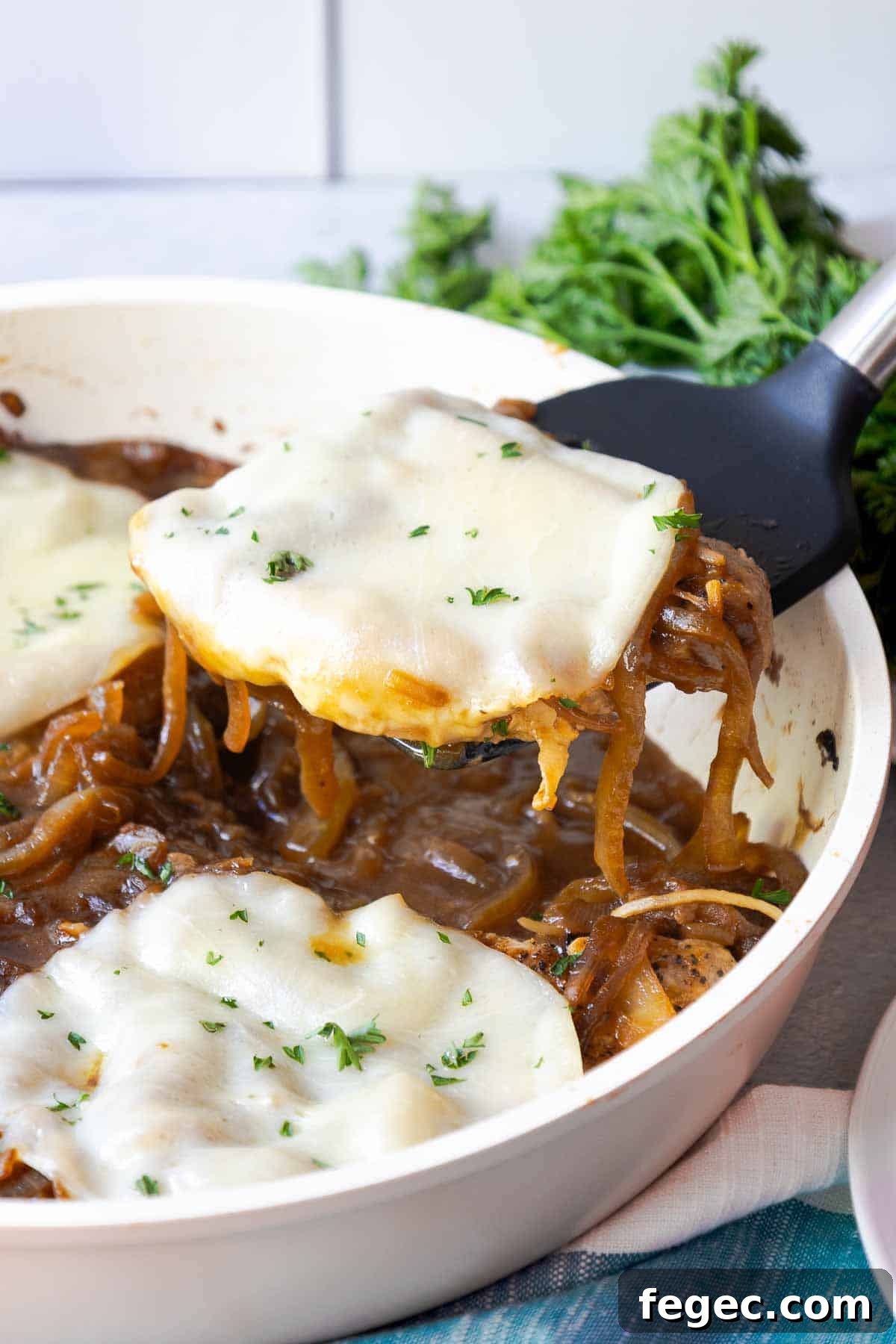 French Onion Pork Chops with Melted Gruyère and Caramelized Onions 14 A pork chop being lifted from a skillet with a spatula, topped with melted provolone and onions.