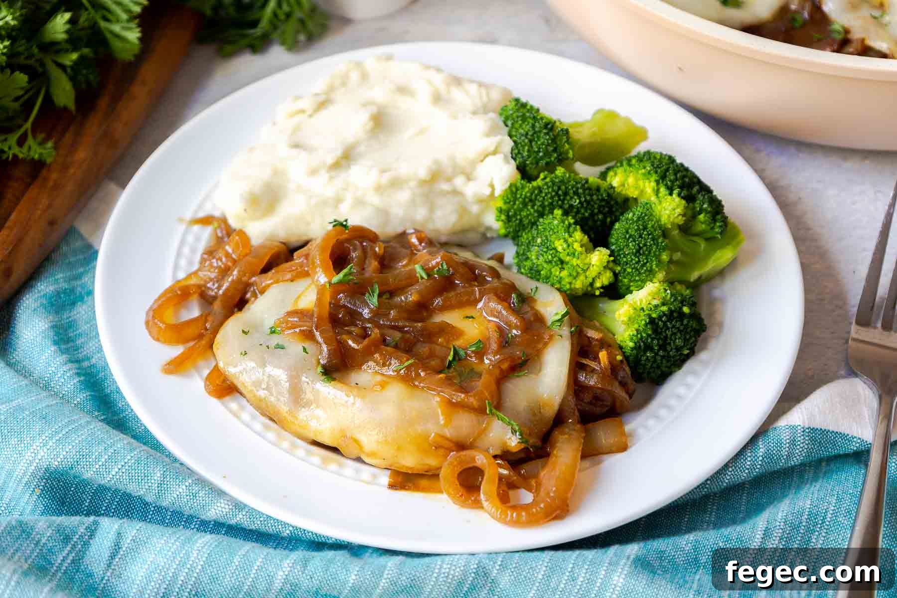 French Onion Pork Chops with Melted Gruyère and Caramelized Onions 15 A pork chop topped with onions and cheese on a plate with mashed potatoes and broccoli.