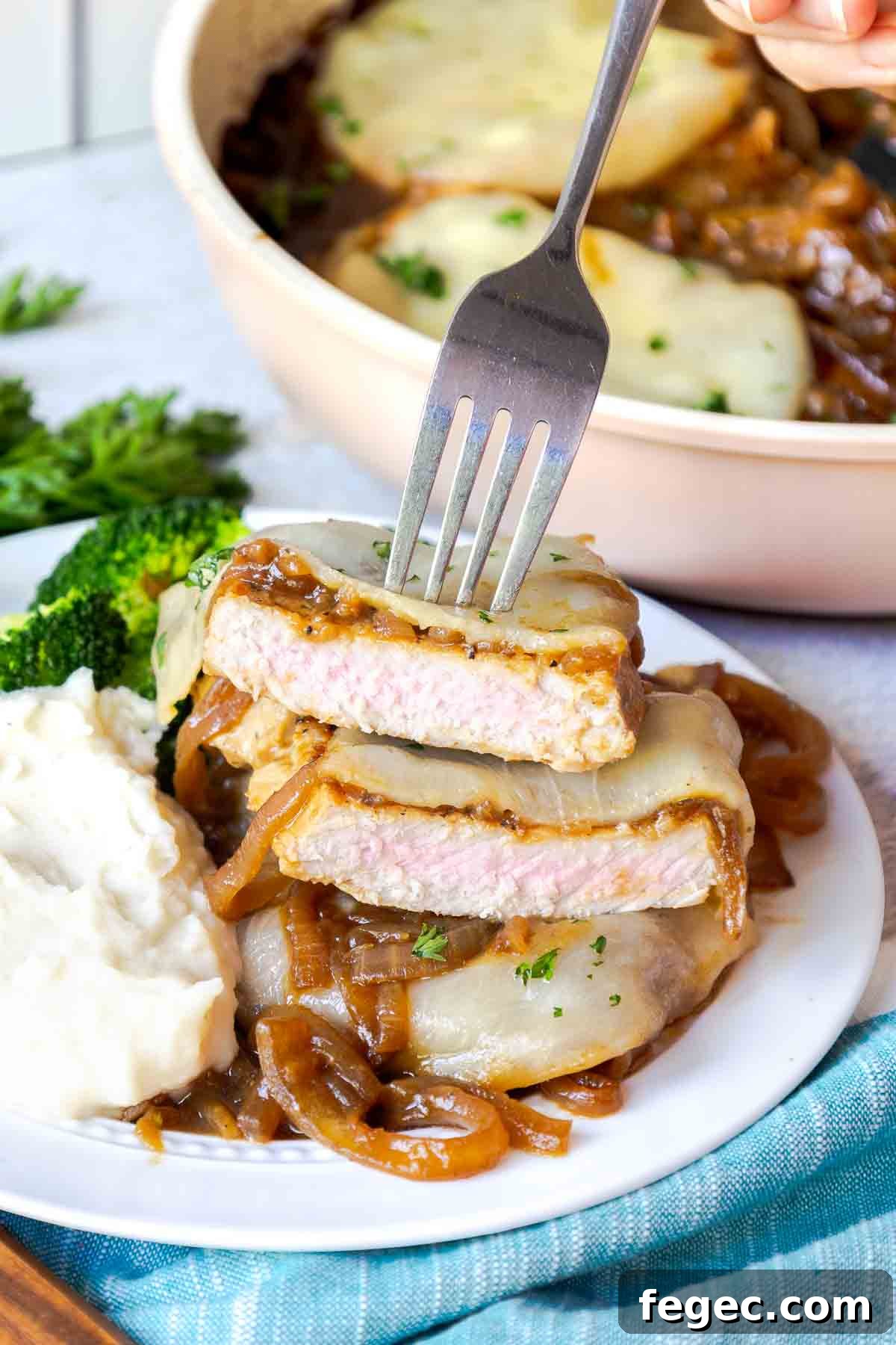 French Onion Pork Chops with Melted Gruyère and Caramelized Onions 3 A sliced pork chop topped with onions and cheese on a plate with mashed potatoes and broccoli.