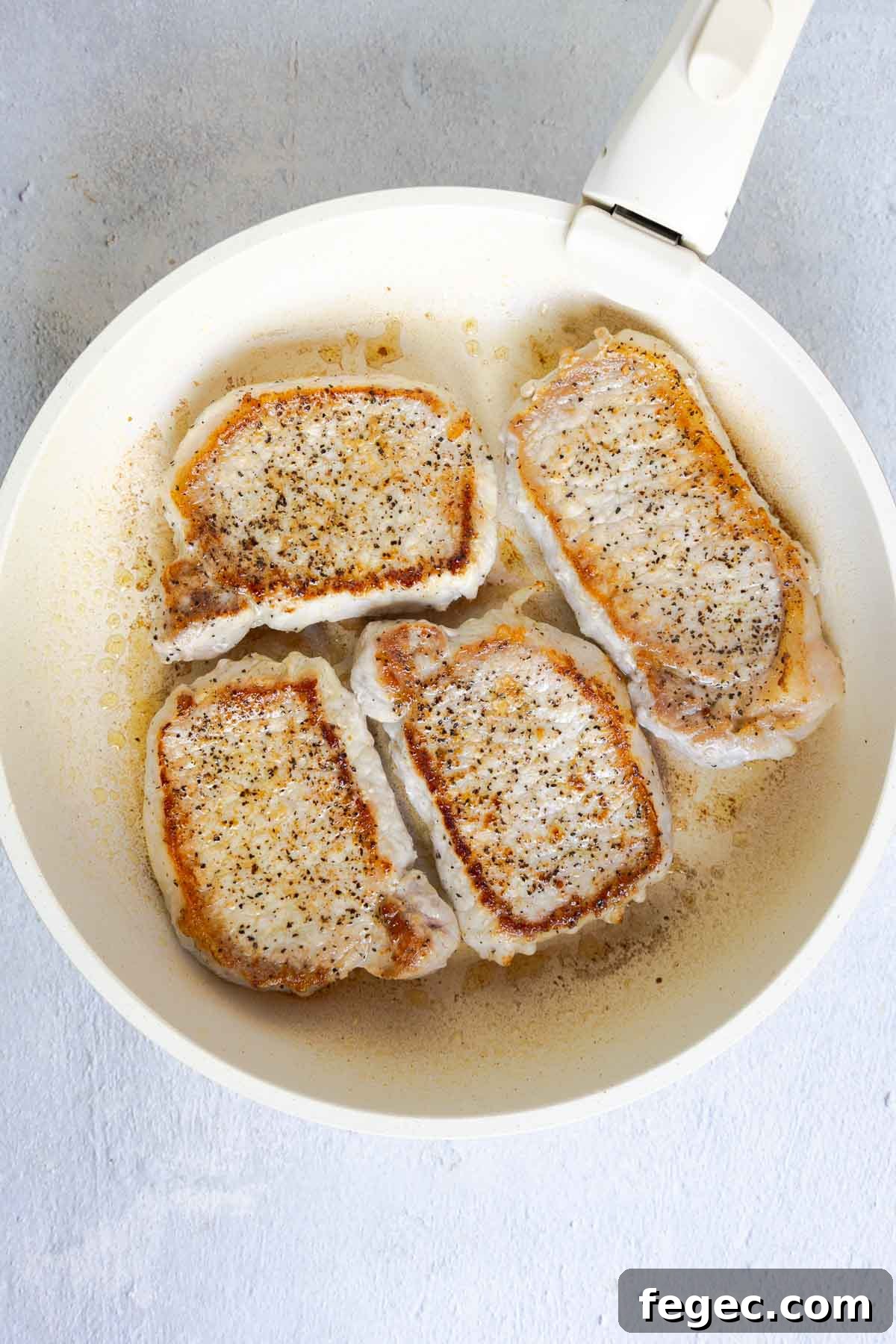 French Onion Pork Chops with Melted Gruyère and Caramelized Onions 6 Four pork chops searing in a skillet until golden.