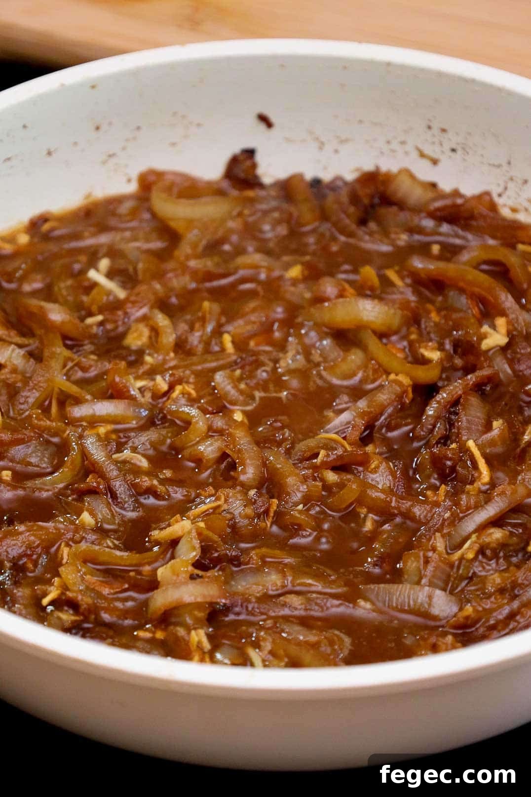 French Onion Pork Chops with Melted Gruyère and Caramelized Onions 9 Caramelized onions simmering in broth in a white skillet.